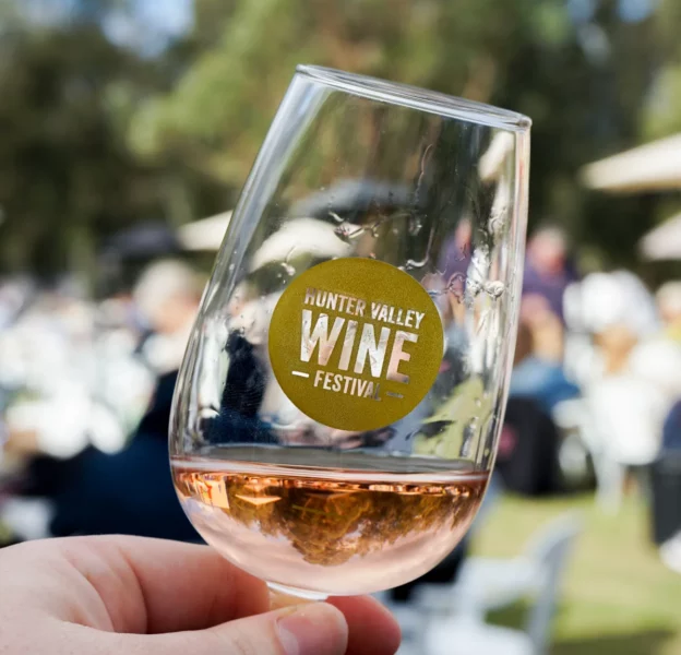 Partly filled wine glass with Hunter Valley Wine Festival logo