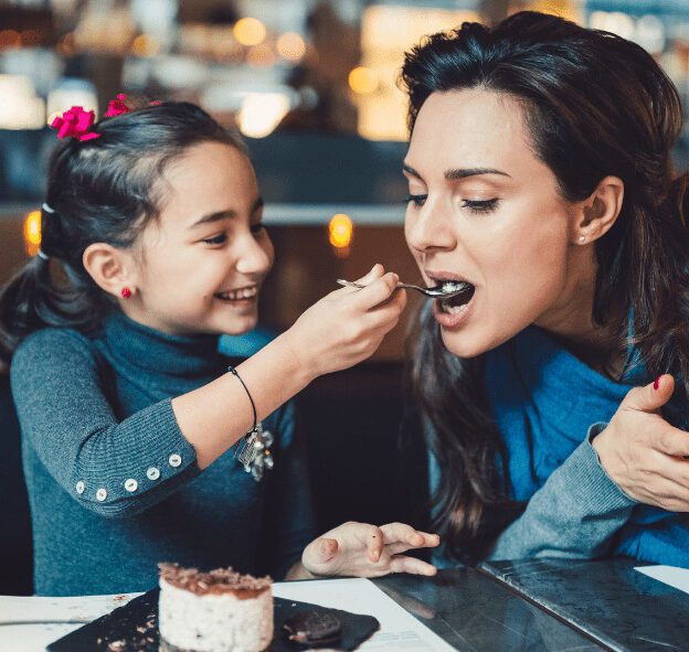 Young girl feeding her mother a spoonful of Oreo cheesecake